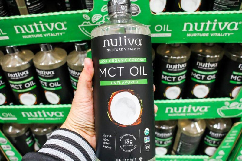 A woman holding a black bottle of MCT oil in a grocery store, in front of other MCT oil bottles