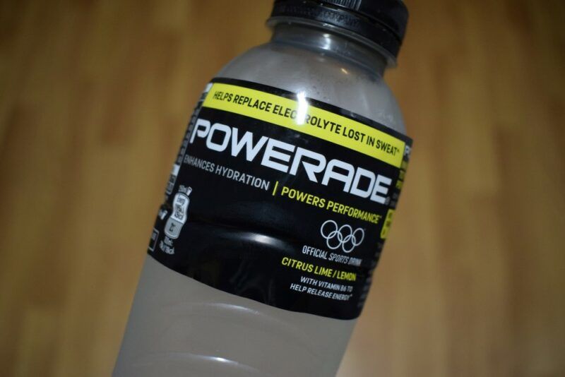 A bottle of lemonade Powerade being held up against a wooden floor