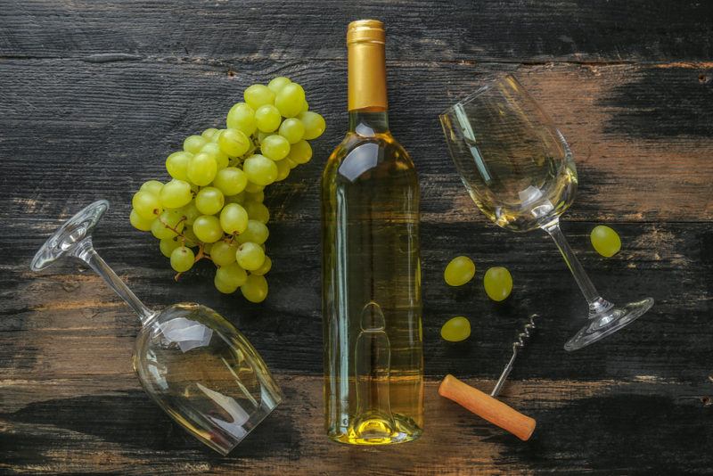 A bottle of chardonnay on a table with two glasses and a bunch of grapes