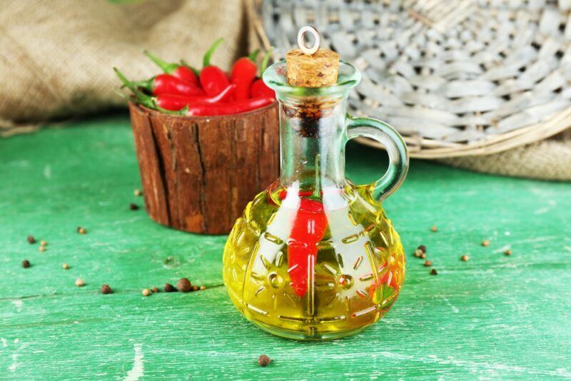 A green table with a jar of chili infused olive oil, next to a wooden container of fresh chilis