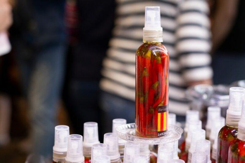 A pile of bottles at a market, with one on top containing chili infused olive oil