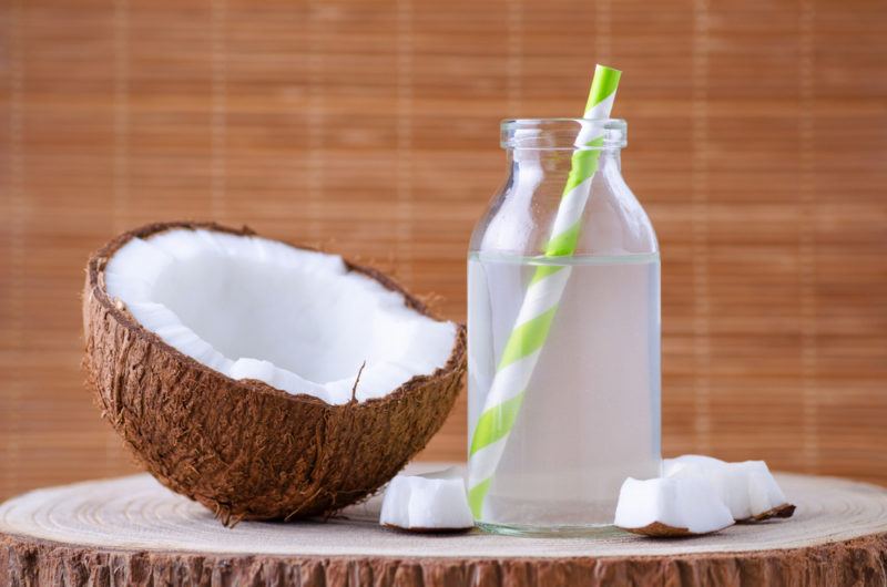 A bottle of coconut water with half of a coconut on a table