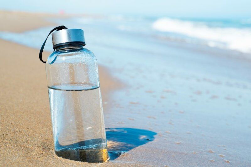 A bottle of filtered water sticking out of the sand on the beach