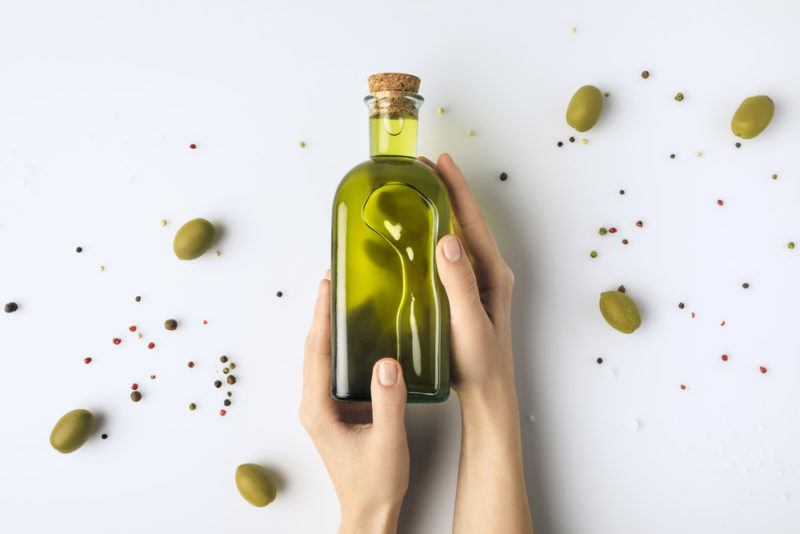 A bottle of olive oil with olives and hands