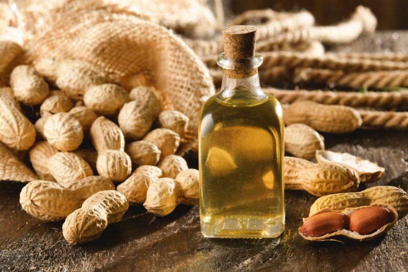 A wooden table with many peanuts in their shells spilling out of a bag, plus a bottle of peanut oil