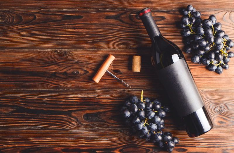 Two bunches of red grapes next to a bottle of red wine, a corkscrew and a cork