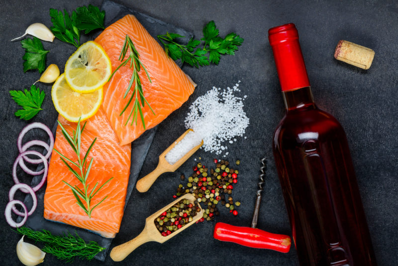 A bottle of pinot noir wine on a table with the raw ingredients for baked salmon, including the fish and various spices