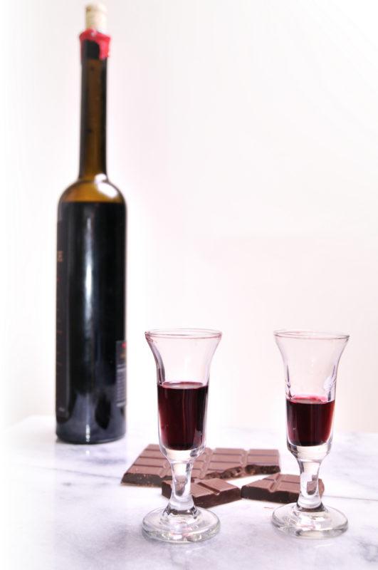 Two glasses of port next to a bottle of port and some milk chocolate