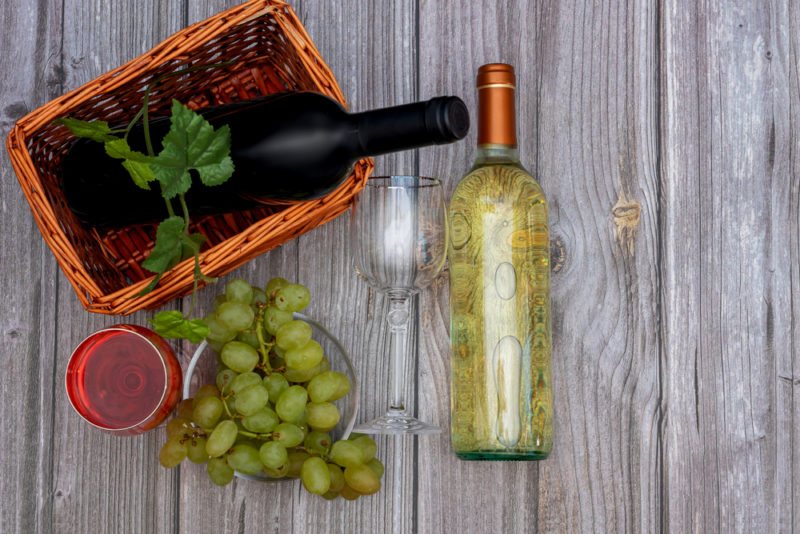 A bottle of red wine and a bottle of chenin blanc with white grapes on a wooden table