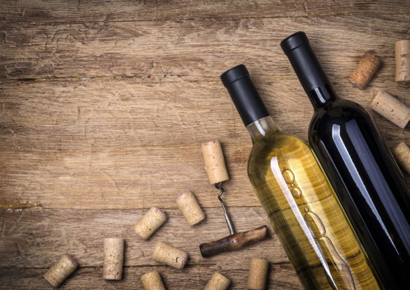 A bottle of red wine, a bottle of wine wine, a corkscrew and corks