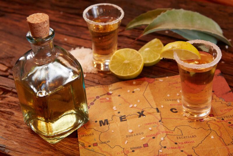 A bottle of tequila, two shot glasses, lime, salt, agave leaves, and a map of Mexico