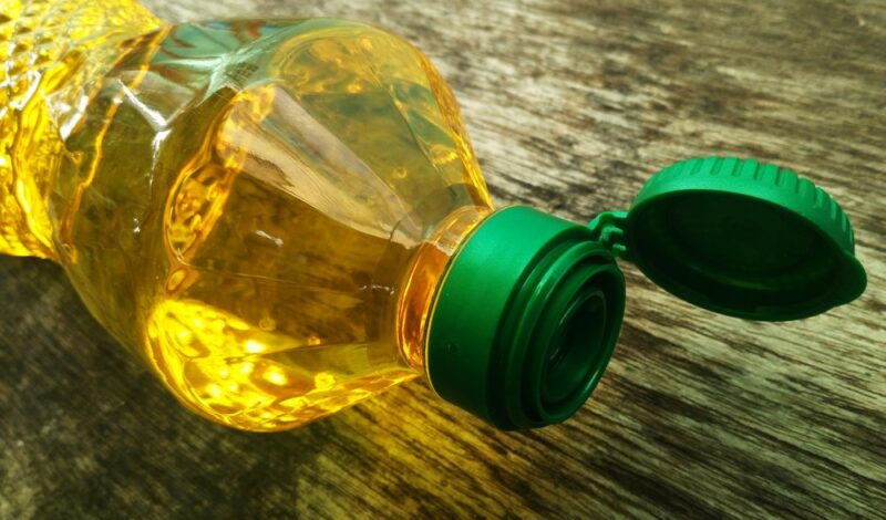 A wooden table with a single bottle of vegetable oil with a green lid on its side