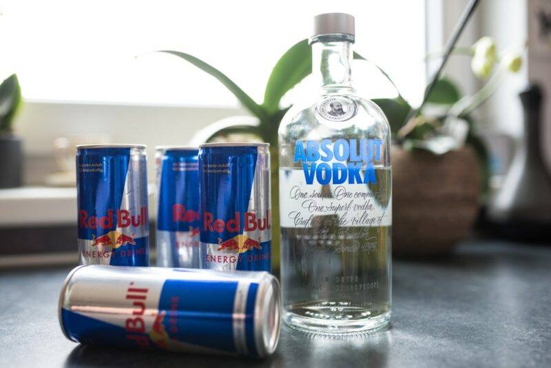 A bottle of vodka on a table, next to cans of Red Bull