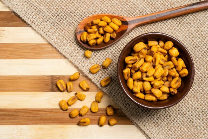 A cloth with a small spoon of corn nuts and a black bowl containing the nuts