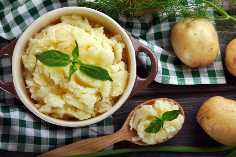 A white dish of mashed potatoes next to a spoon of the potatoes