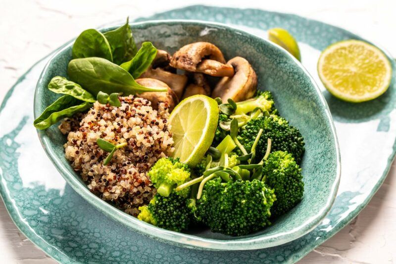 A teal bowl containing a savory meal that includes quinoa, mushrooms, and broccoli