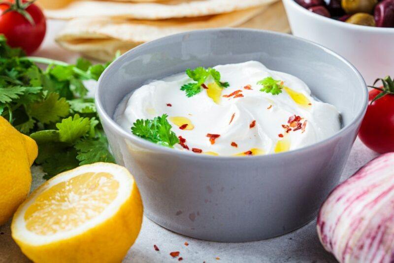 A gray bowl containing whipped feta dip, next two lemon halves and herbs