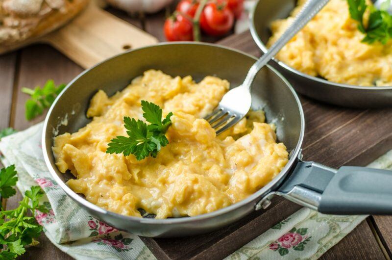 A small pan that contains scrambled eggs, with a piece of parsley and a fork