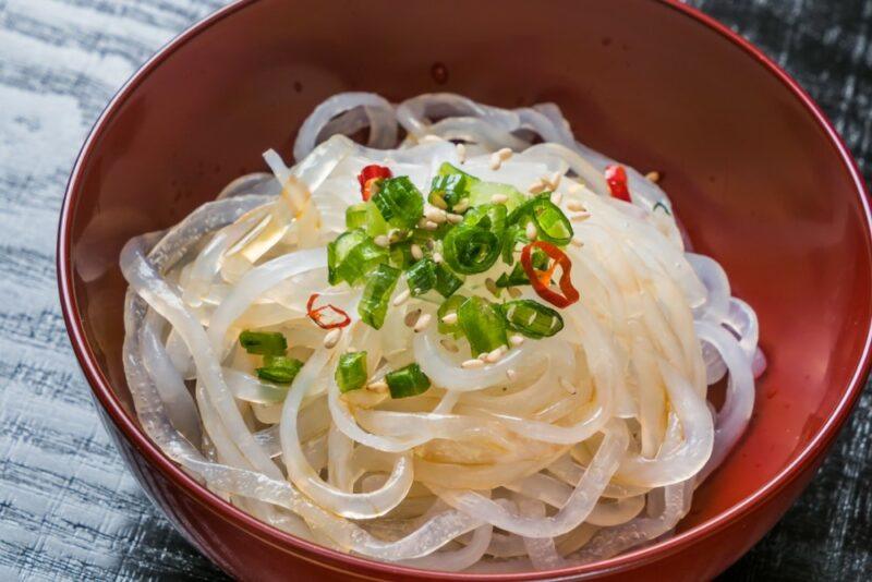 A brown bowl containing cooked shirataki noodles with spring onions on top