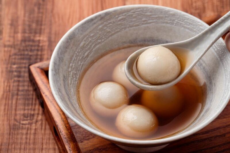 A bowl of tangyuan in broth, where a spoon is being used to scoop one out