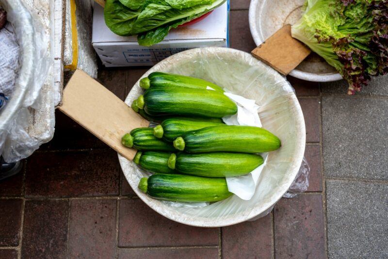 A wooden table containing a large bowl of zucchinis that are being sold in a Korean market