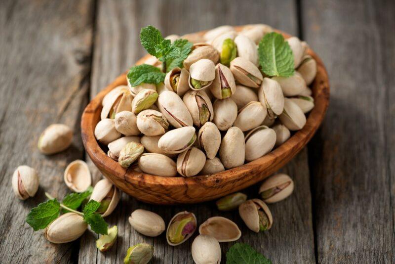 A bowl filled with pistachios | Food For Net A brown bowl of pistachio nuts still in their shells on a wooden table