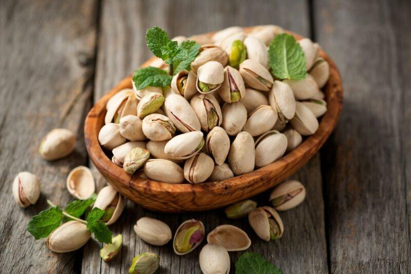 A brown bowl of pistachio nuts still in their shells on a wooden table