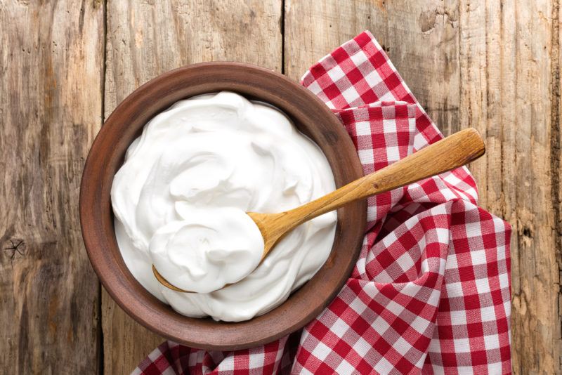 A bowl full of yogurt on a wooden table with a red and white cloth