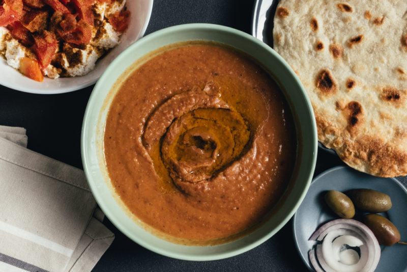 A light bowl filled with fool, next to pita and another dip