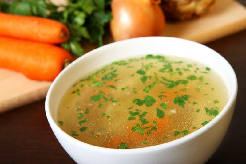 A large white bowl of broth-based soup, with carrots, onions and everything else