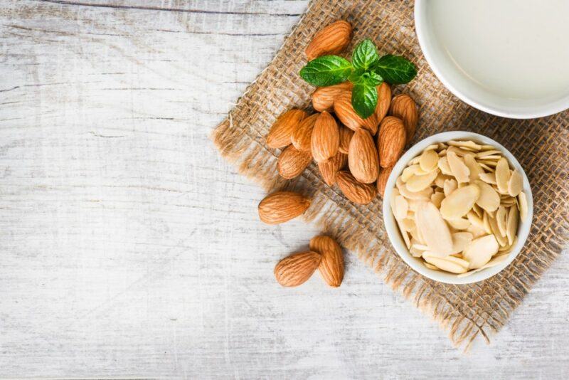 A cloth with almonds, next to a small bowl of almond slices and a bowl of almond milk