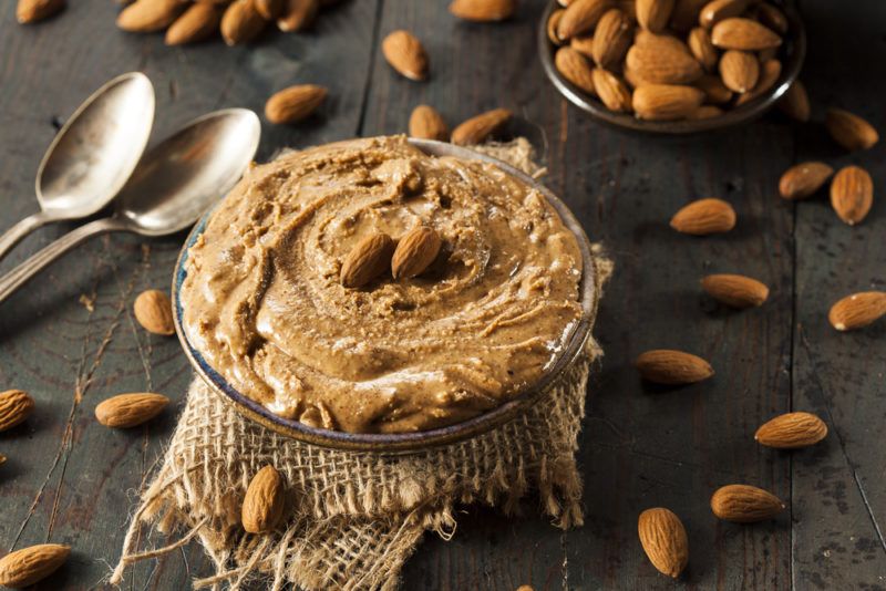 A glass bowl with almond butter, where almonds are scattered across the table