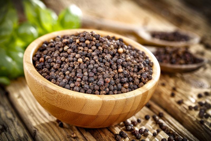 A wooden bowl that contains black peppercorns