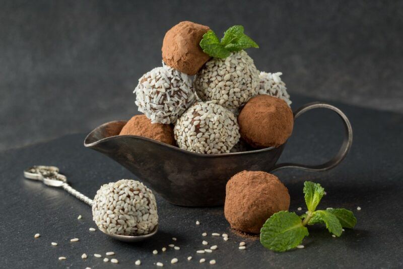 A black dish containing bliss balls. Some are rolled in coconut and others are rolled in cocoa