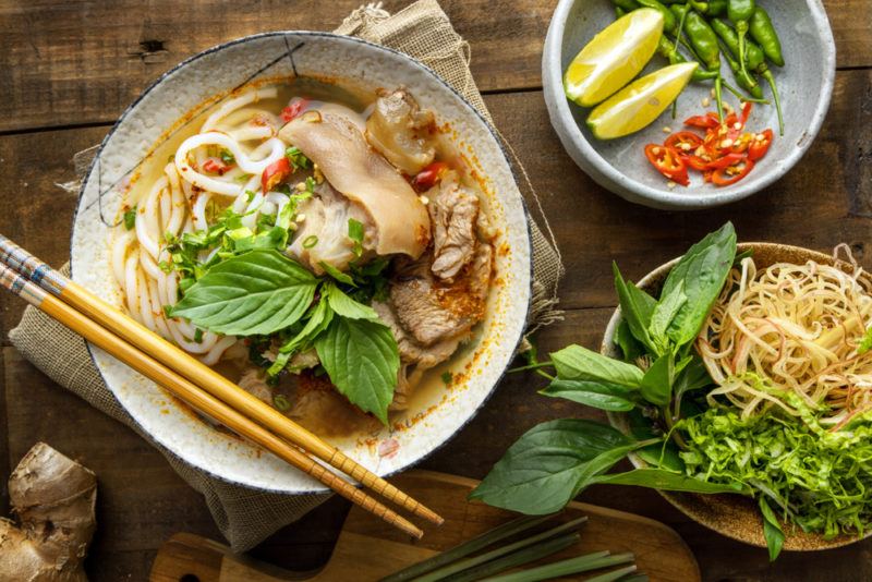 A dish on the table that contains a dish of bun bo or bun bo hue, next to a bowl of vegetables and another of noodles and vegetables