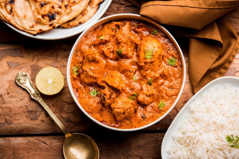 A bowl of butter chicken next to a bowl of rice and some naan bread