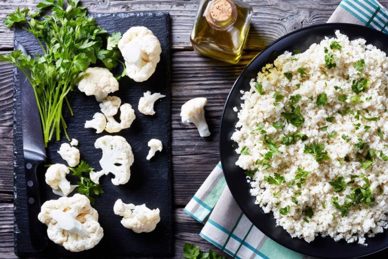 A black bowl of cauliflower rice, next to a black dish of cauliflower