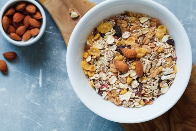 A white bowl of cereal next to a small bowl of nuts on a table