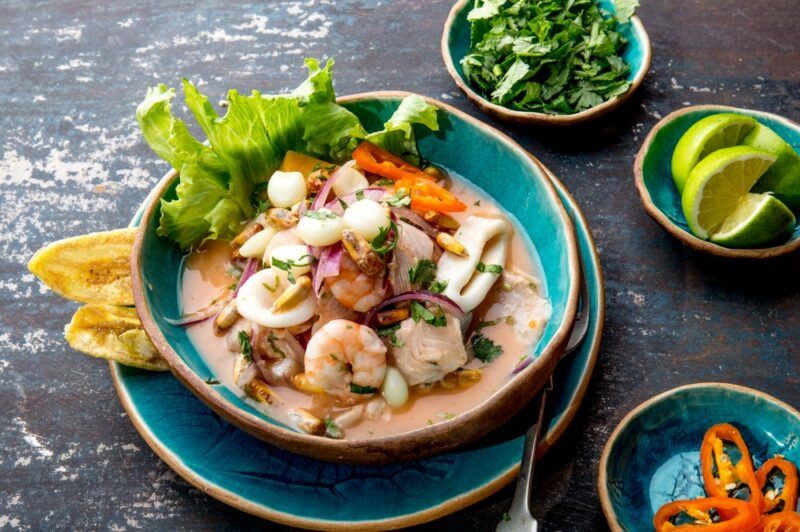 A blue dish of ceviche, next to small bowls containing toppings