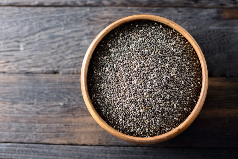 A brown bowl of chia seeds on a wooden floor