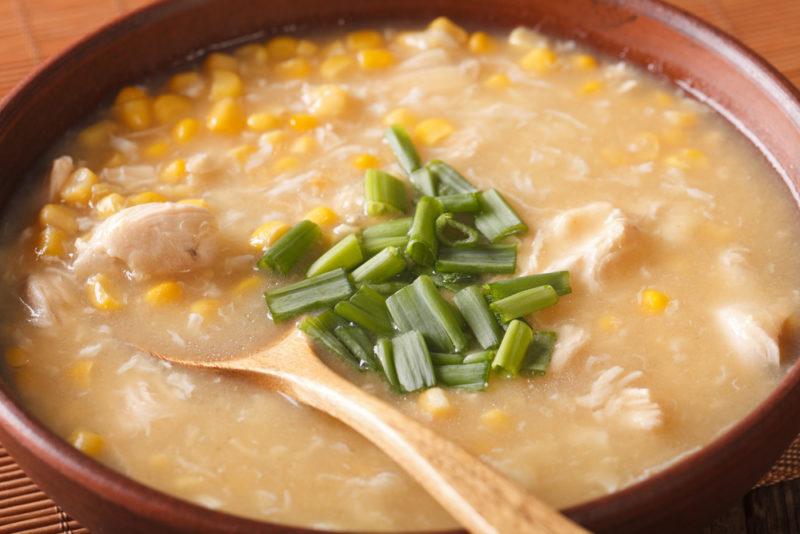 A bowl of chicken and corn chowder with greens in the middle and a wooden spoon