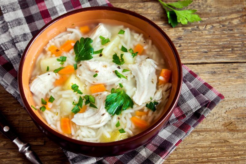 A bowl of chicken noodle soup with vegetables on top of a teatowel