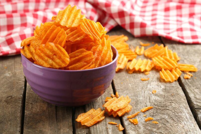 A wooden table with chips, with a purple bowl with even more chips piled high