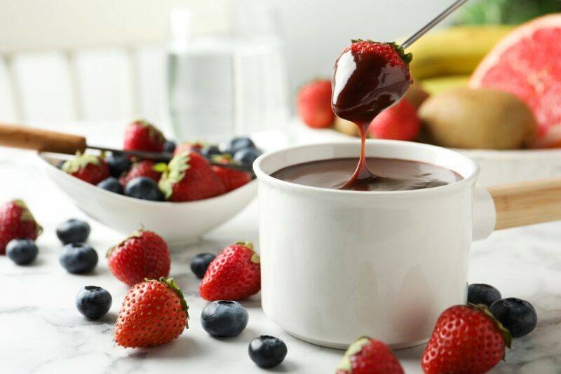 A white pot of chocolate sauce with fresh fruit