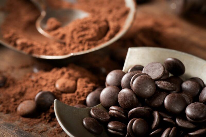 A small container of black chocolate pieces, with a bowl of cocoa powder