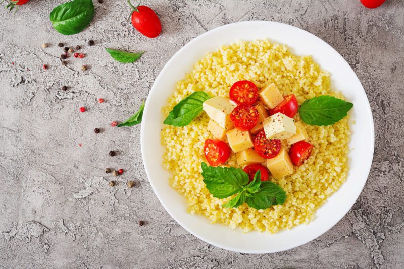 A white bowl with cooked millet, tomatoes, and cheese