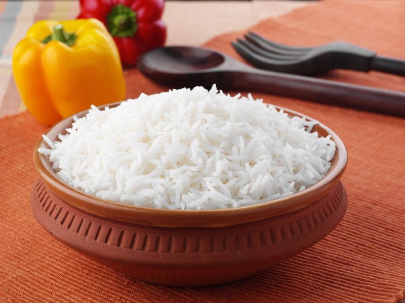 A terracotta dish of cooked rice, with peppers and cutlery in the background