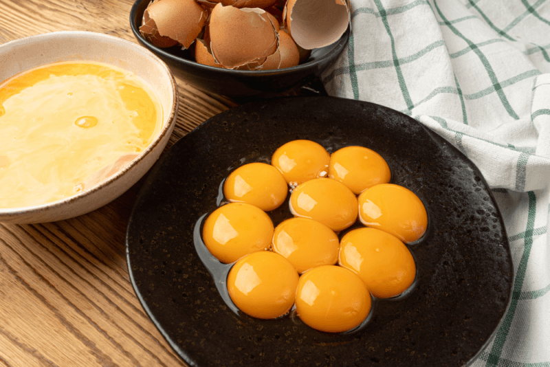 A black plate with egg yolks, a bowl of egg whites, and a bowl of empty egg shells