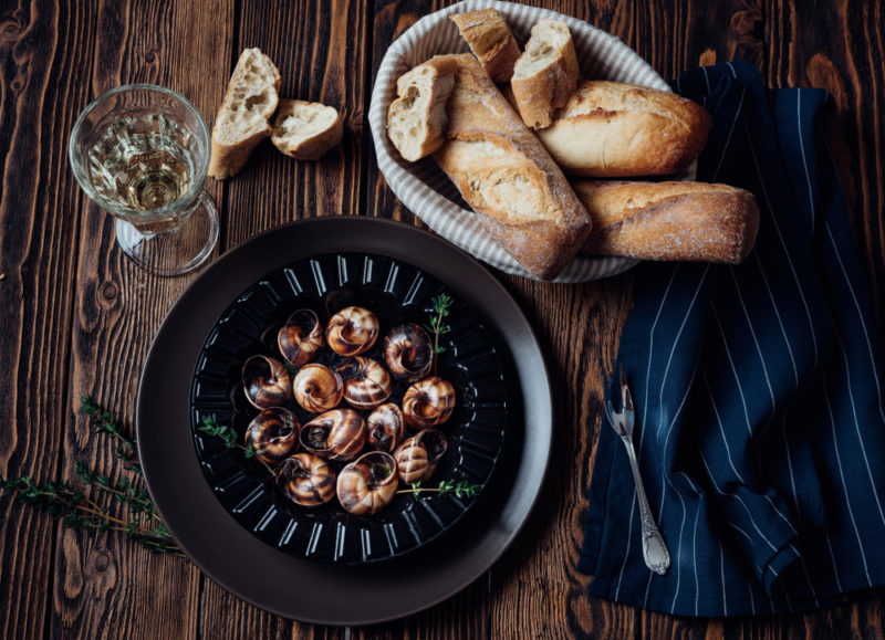 A black plate with escargot next to a bowl of bread