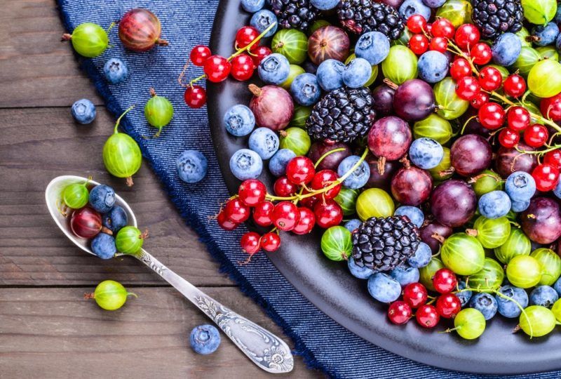 A blue dish containing a selection of unusual berries, including currants and kiwiberries. A few more are scattered on the table